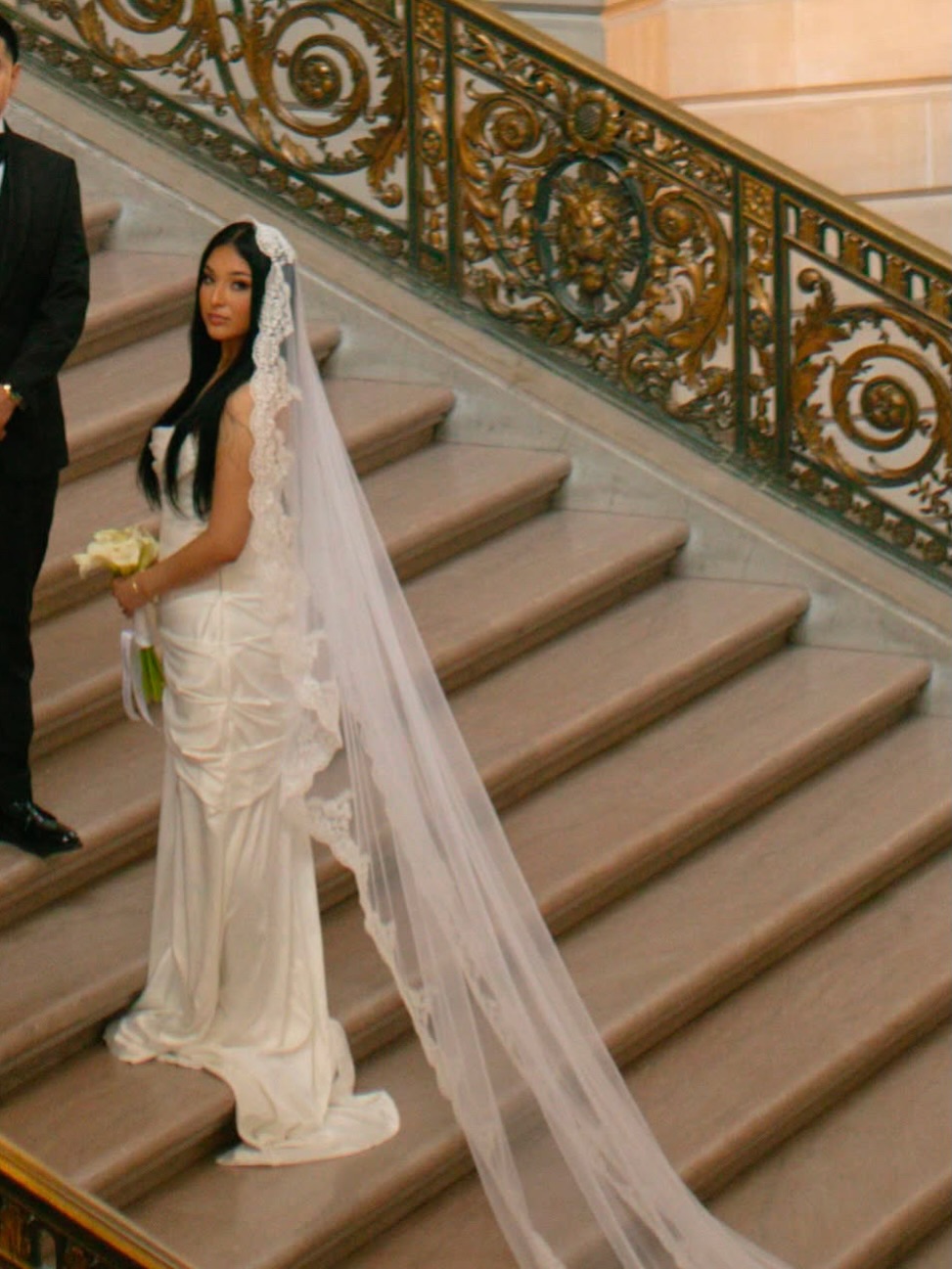 Bride in a white gown and long veil on an ornate staircase