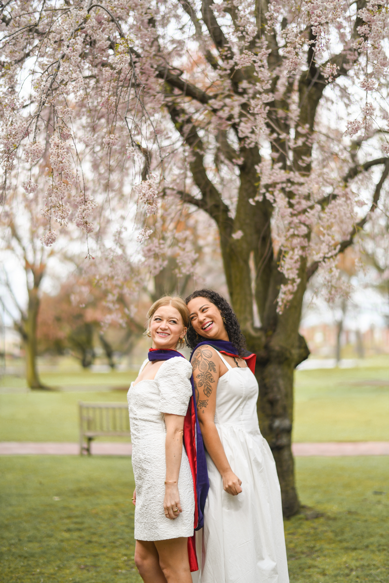 Two graduates smiling beneath flowering branches