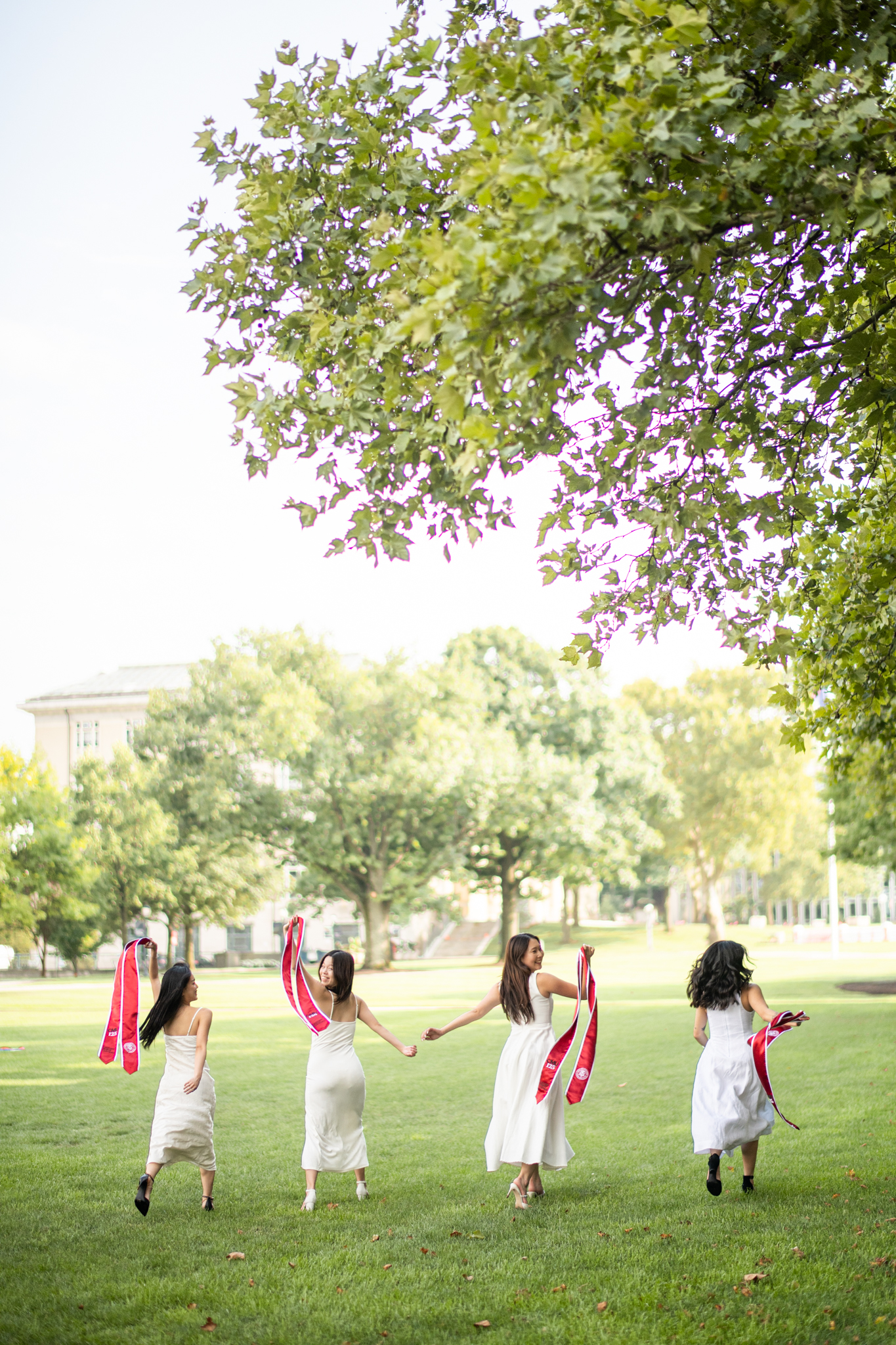 Four graduates running together across a green campus lawn